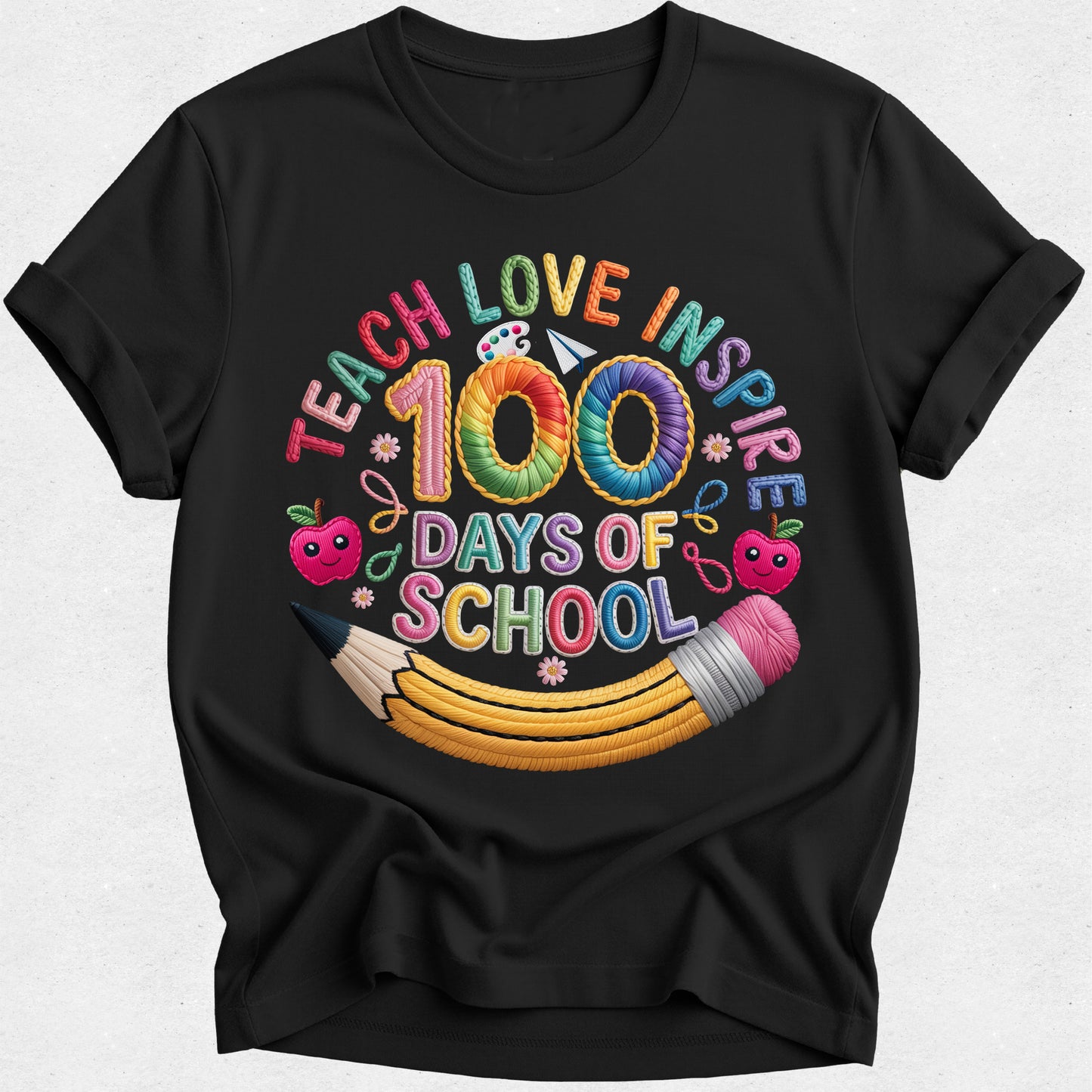 A black short-sleeve crewneck t-shirt with a colorful graphic on the front reading 'TEACH LOVE INSPIRE 100 DAYS OF SCHOOL' in rainbow-colored letters, decorated with cartoon apples and a yellow pencil.