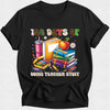 A black short-sleeve crewneck t-shirt featuring a colorful graphic design on the front. The graphic displays the text '100 DAYS OF DOING TEACHER STUFF' with school-themed illustrations including books, a pink drink, a yellow folder, a red apple, and crayons.