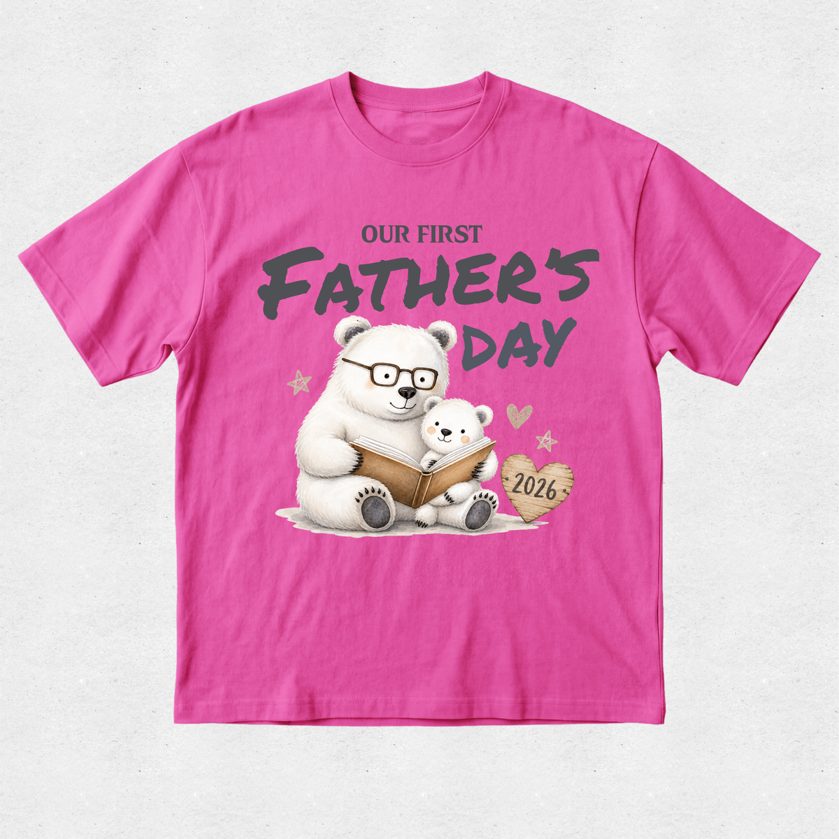 A bright pink short-sleeve t-shirt with a graphic on the front showing two polar bears reading a book, with the text 'OUR FIRST FATHER'S DAY' and '2026'.