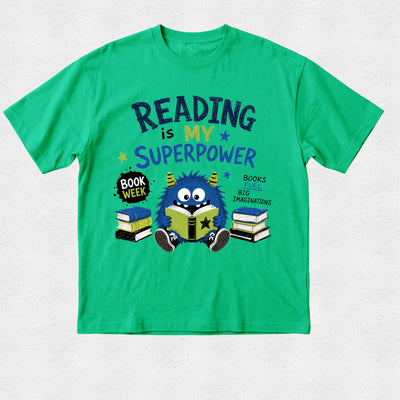 A bright green short-sleeve t-shirt with a colorful graphic on the front. The graphic features the text 'READING is MY SUPERPOWER' in dark blue and purple lettering, along with a cartoon blue monster reading a book, surrounded by stacks of books and a 'BOOK WEEK' badge.