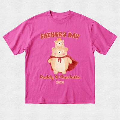 A bright pink short-sleeve t-shirt with a custom graphic on the front. The graphic features two cartoon teddy bears, one wearing a red cape and the other sitting on its shoulders, with the text 'FATHERS DAY' above and 'Daddy & Charlotte 2026' below in a warm orange-brown font.