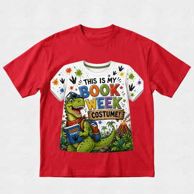 A red short-sleeve crewneck t-shirt featuring a colorful graphic print on the front. The graphic shows a green cartoon dinosaur wearing blue glasses and a red bandana, holding a book, with the text 'THIS IS MY BOOK WEEK COSTUME!' in multicolored letters.