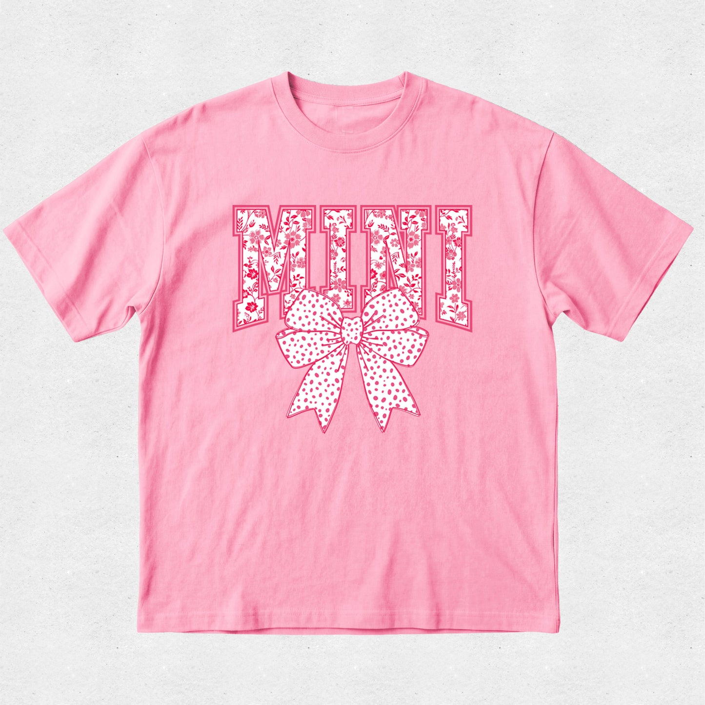 Pink t-shirt with decorative text and bow design on a light gray background