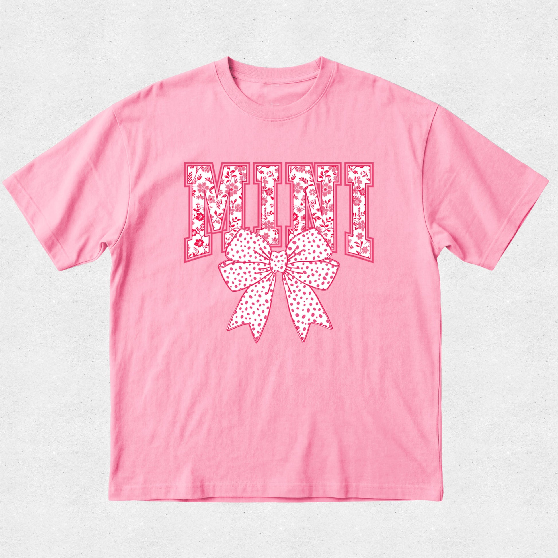 Pink t-shirt with decorative text and bow design on a light gray background