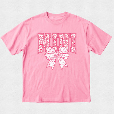 Pink t-shirt with decorative text and bow design on a light gray background