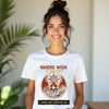 Woman wearing a white t-shirt with NAIDOC Week design, standing indoors with plants in the background.