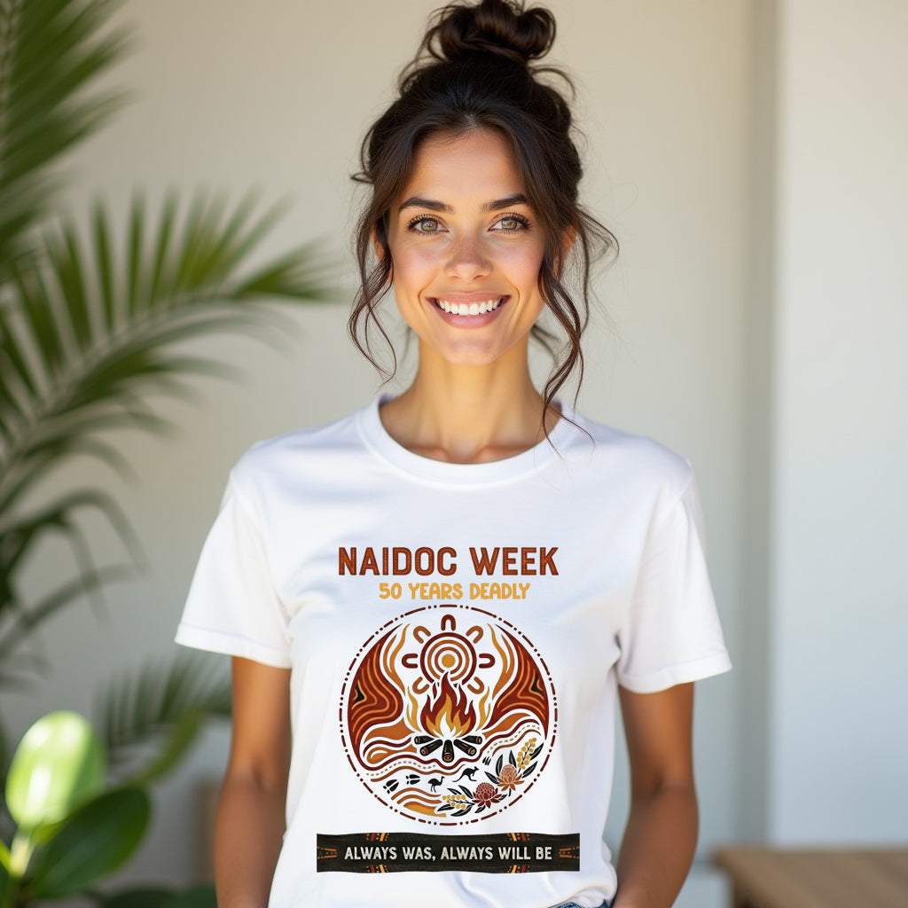 Woman wearing a white t-shirt with NAIDOC Week design, standing indoors with plants in the background.