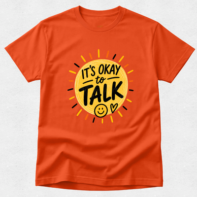 An orange short-sleeve crewneck t-shirt featuring a graphic design of a yellow sun with the text 'IT'S OKAY to TALK' and a smiley face, displayed on a light gray textured background.