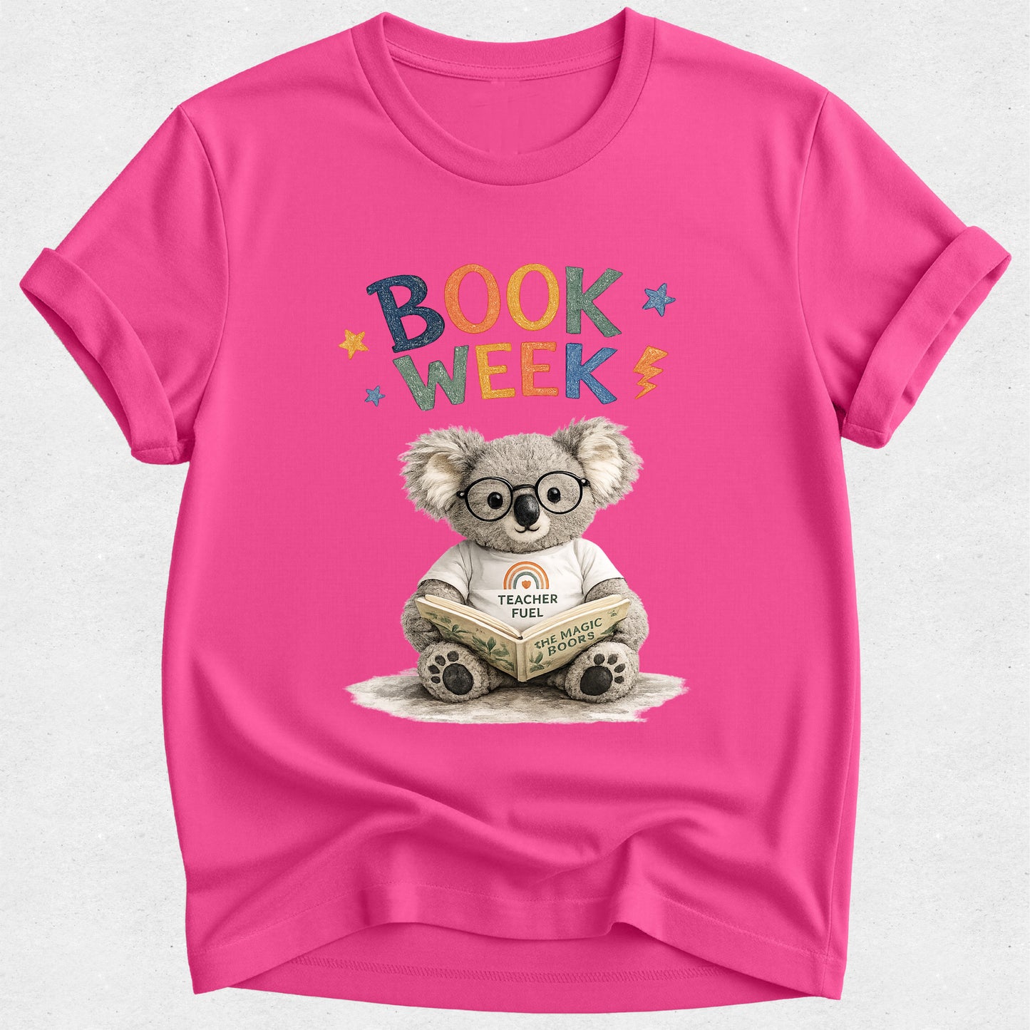 A bright pink short-sleeve t-shirt with a 'Book Week' graphic featuring a cartoon koala wearing glasses and reading a book, displayed on a light gray textured background.
