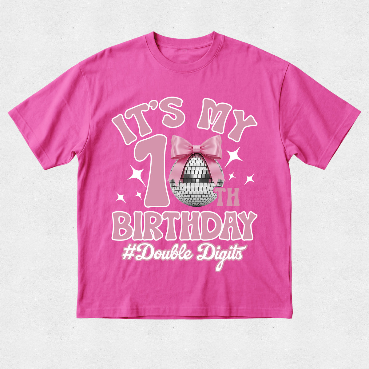 A bright pink short-sleeve t-shirt with a '1st Birthday' graphic on the front, featuring a pink bow, disco ball, and the text '#Double Digits' on a light gray textured background.