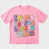 A pink short-sleeve t-shirt with a colorful retro-style graphic on the front that reads 'IN MY DOUBLE DIGITS ERA' in bubbly, polka-dotted letters, displayed flat against a light gray textured background.