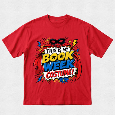 A red short-sleeve crewneck t-shirt featuring a colorful comic book style graphic that reads 'THIS IS MY BOOK WEEK COSTUME!' with a superhero mask, cape, and comic-style text elements.
