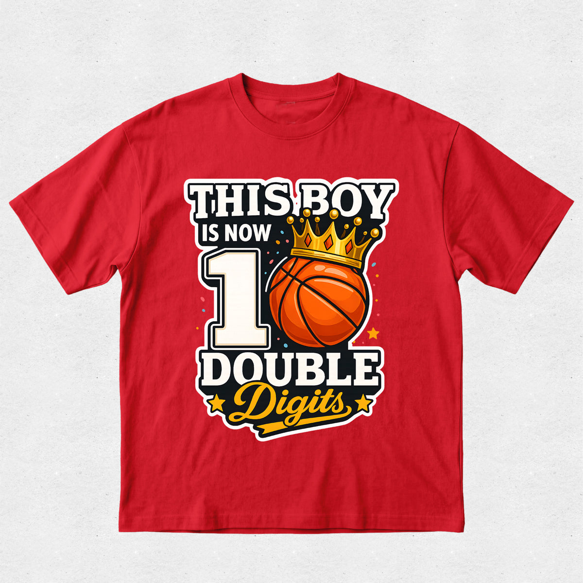 A red short-sleeve crewneck t-shirt with a graphic print on the front. The graphic features the text 'THIS BOY IS NOW 10 DOUBLE Digits' in white, black, and yellow lettering, accompanied by an illustration of an orange basketball wearing a gold crown.