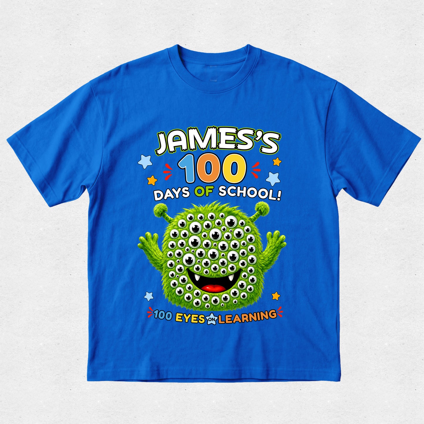 A bright blue short-sleeve t-shirt with a colorful graphic on the front reading 'JAMES'S 100 DAYS OF SCHOOL! 100 EYES LEARNING!' above and below a green cartoon monster with many eyes, shown on a light gray background.