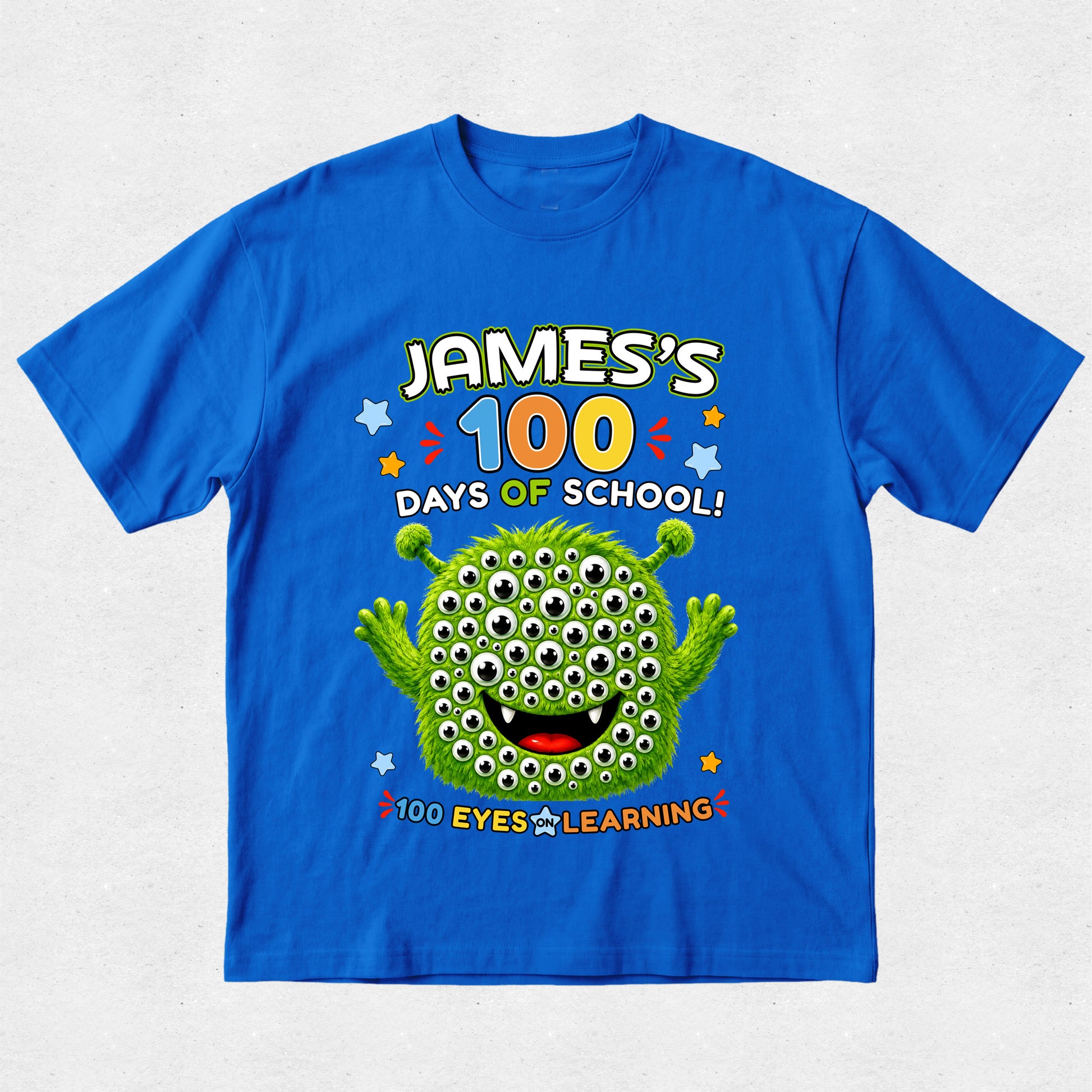 A bright blue short-sleeve t-shirt with a colorful graphic on the front reading 'JAMES'S 100 DAYS OF SCHOOL! 100 EYES LEARNING!' above and below a green cartoon monster with many eyes, shown on a light gray background.