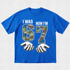 Blue t-shirt with camouflage numbers '6' and '7' and text 'I WAS 6 NOW I'M 7' on a light gray background