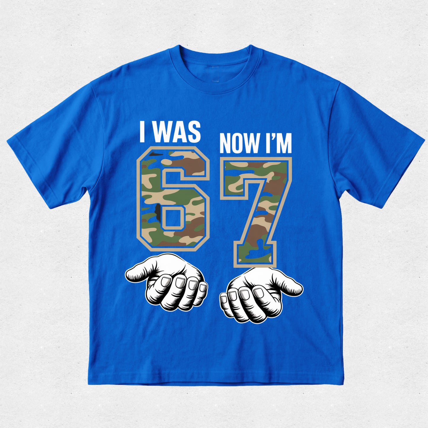 Blue t-shirt with camouflage numbers '6' and '7' and text 'I WAS 6 NOW I'M 7' on a light gray background