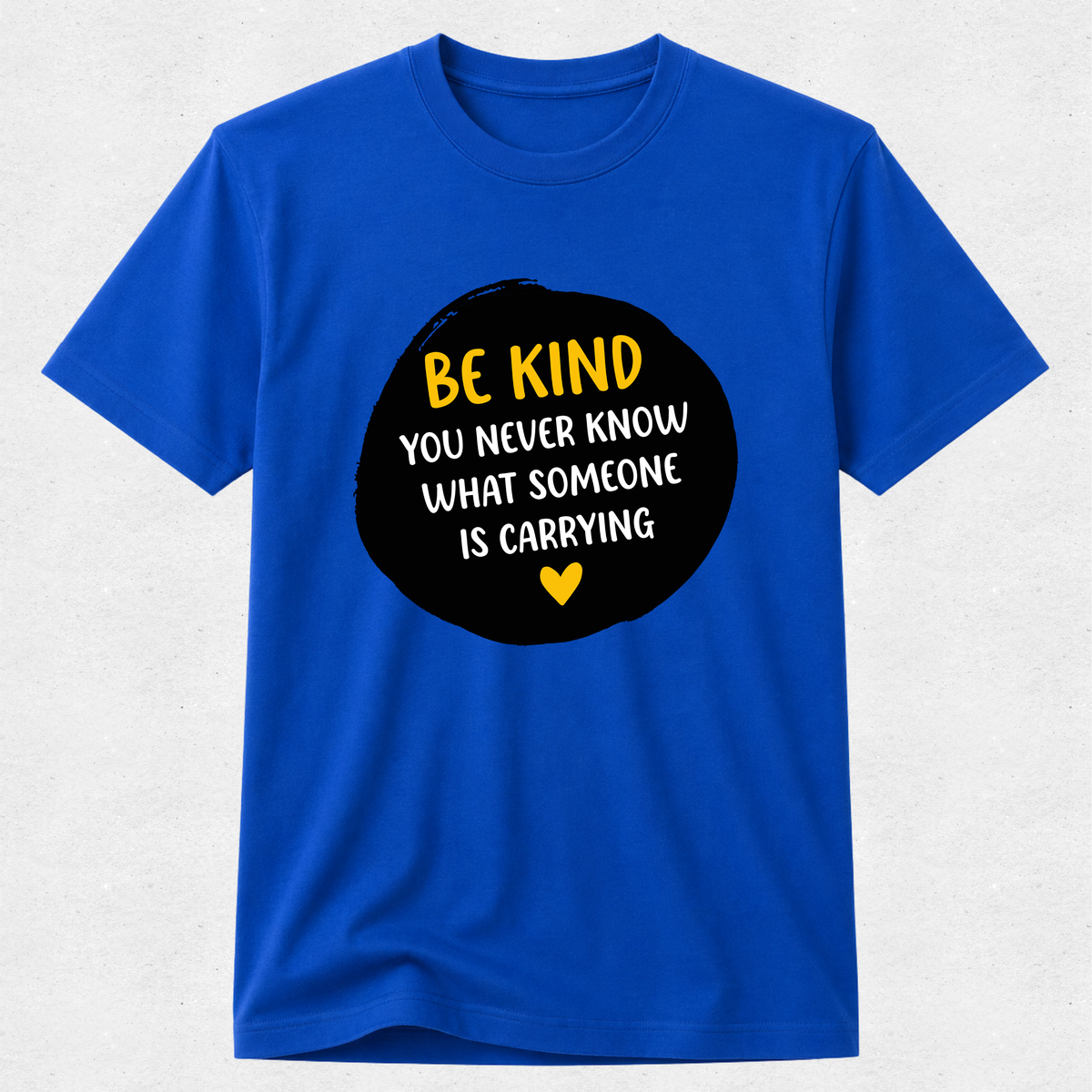A royal blue short-sleeve t-shirt with a black circular graphic on the chest containing the text 'BE KIND YOU NEVER KNOW WHAT SOMEONE IS CARRYING' in yellow and white, with a small yellow heart at the bottom.
