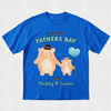 A royal blue short-sleeve t-shirt with a custom Father's Day graphic featuring two cartoon bears holding hands and a light blue heart-shaped balloon. The text reads 'OUR FIRST FATHER'S DAY', '2026', and 'Daddy & Lucas'.