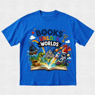 A bright blue short-sleeve t-shirt with a colorful graphic print on the front. The graphic features the text 'BOOKS UNLOCK WORLDS' above an open book with various whimsical illustrations including a castle, rainbow, dinosaur, rocket ship, dragon, and treasure chest, all set against a light gray textured background.