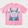 A pink short-sleeve crewneck t-shirt featuring a colorful graphic of a mermaid in a book-themed costume with the text 'THIS IS MY BOOK WEEK COSTUME!'.