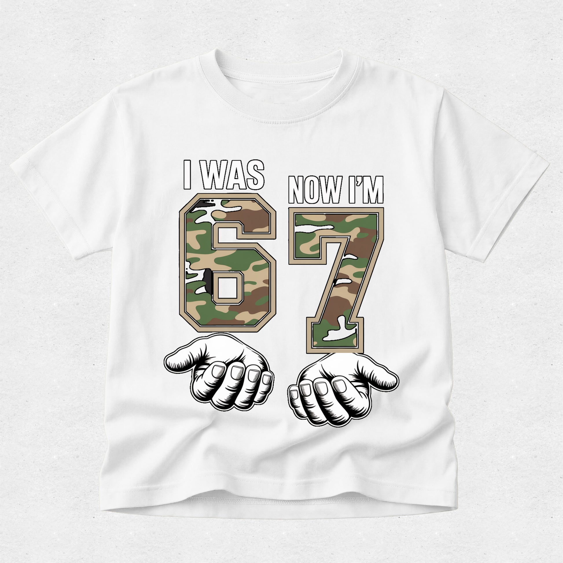 White t-shirt with camouflage numbers '67' and fists, text 'I was 67 now I'm', on a white background.