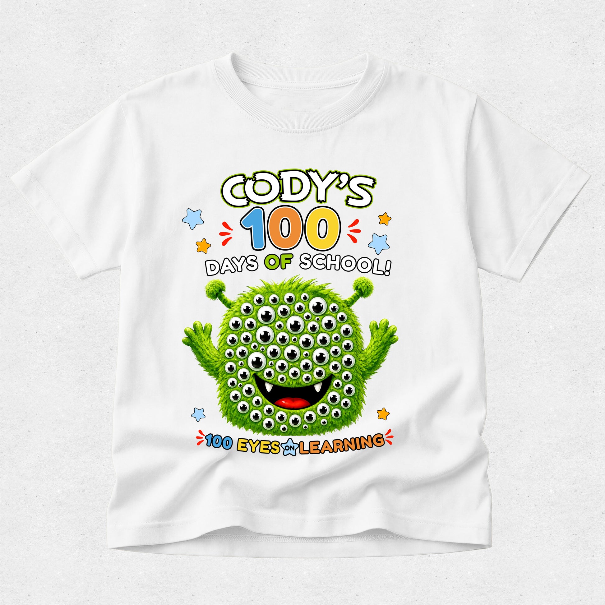 A white short-sleeve kids' t-shirt with a colorful graphic on the front. The graphic features a green cartoon monster with many eyes and the text 'CODY'S 100 DAYS OF SCHOOL! 100 EYES LEARNING'.