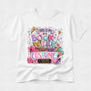 A white short-sleeve crewneck t-shirt featuring a colorful graphic print on the front that reads 'THIS IS MY BOOK WEEK COSTUME!' surrounded by illustrations of a crown, pink heels, a wand, and shopping bags.
