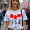 Woman wearing a white t-shirt with red poppy flowers and text in a busy street.