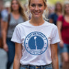 Woman wearing a white t-shirt with a blue 'Lest We Forget' design in a crowd.