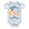 A white short-sleeve baby bodysuit with a custom 'Our First Fathers Day' graphic. The graphic features two watercolor-style teddy bears holding hands, one larger bear wearing a black top hat and one smaller bear wearing a small gold crown, holding a light blue balloon.