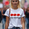 Woman wearing a white t-shirt with red poppies and 'Lest We Forget' text in a crowd.