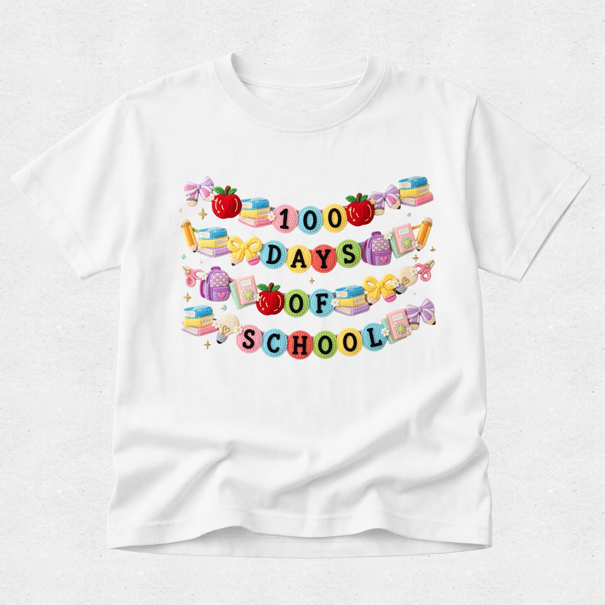 A white short-sleeve crewneck t-shirt featuring a colorful graphic on the front that reads '1000 DAYS OF SCHOOL' in pastel lettering, decorated with school-themed illustrations like apples, books, and pencils.