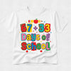 A white short-sleeve t-shirt with a colorful graphic that reads '67 + 33 Days of School' in playful multicolored letters, decorated with a pencil, apple, and leopard-print patterned letters, shown on a light gray background.
