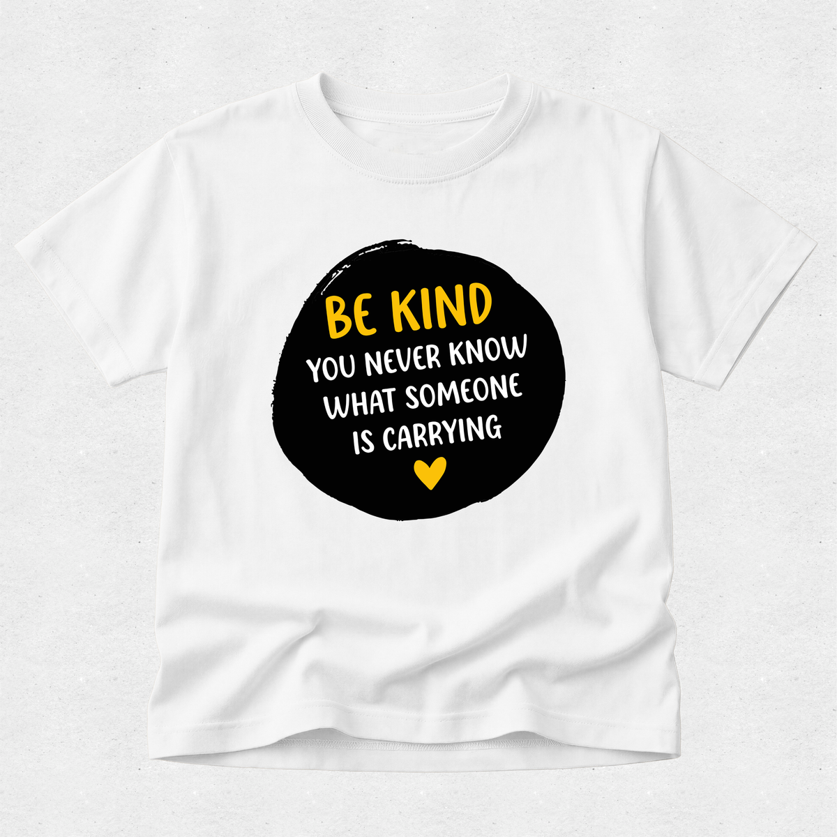 A white short-sleeve crewneck t-shirt with a black circular graphic on the chest containing the text 'BE KIND YOU NEVER KNOW WHAT SOMEONE IS CARRYING' in yellow and white, with a small yellow heart below.