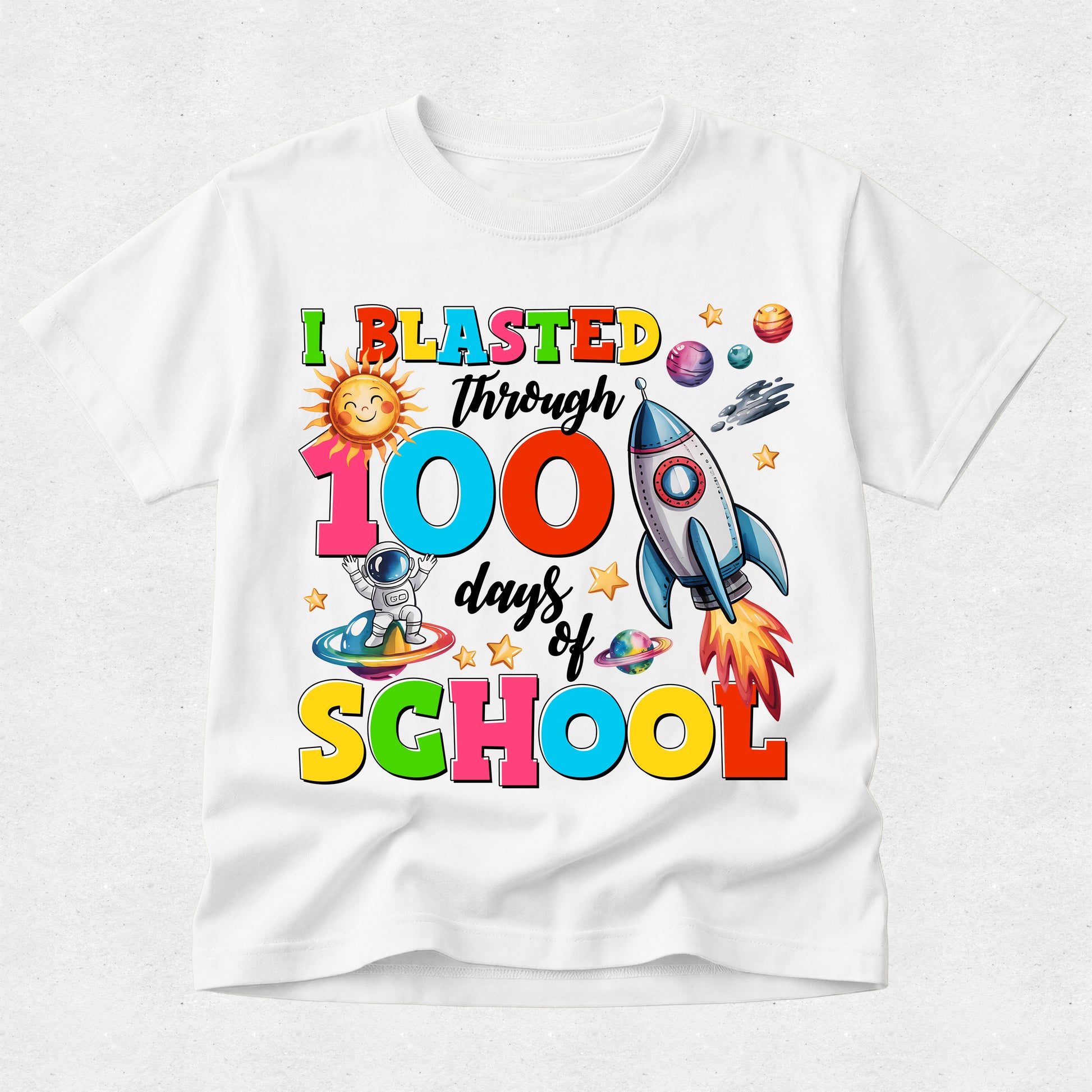 A white short-sleeve crewneck t-shirt featuring a colorful graphic print on the front that reads 'I BLASTED through 100 days of SCHOOL' with cartoon illustrations of a sun, astronaut, rocket ship, and planets.