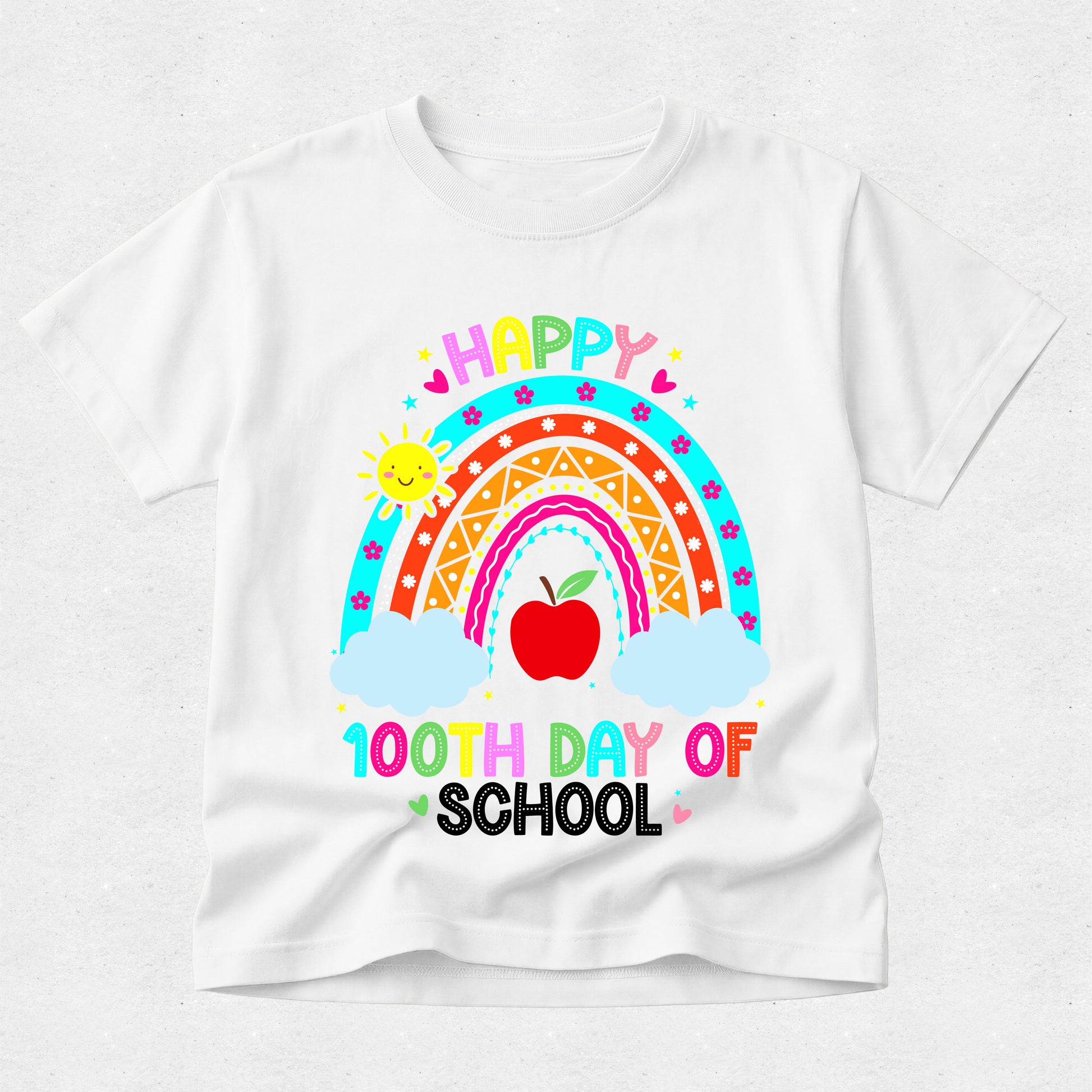 A white short-sleeve t-shirt with a colorful graphic celebrating a 100th day of school, featuring a rainbow, red apple, clouds, and the text 'HAPPY 100TH DAY OF SCHOOL'.