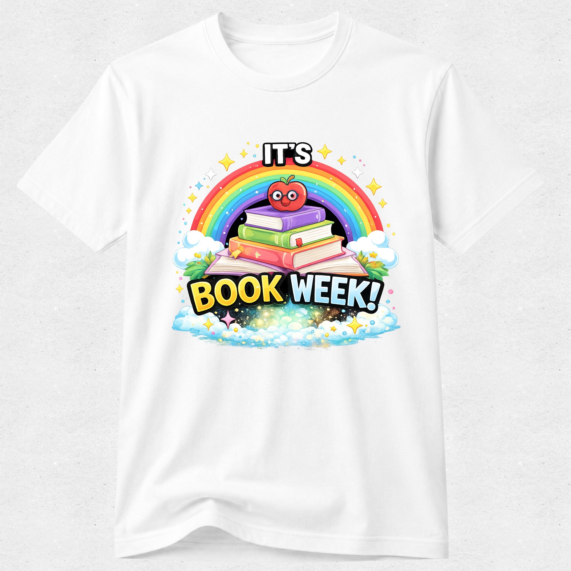 A white short-sleeve crewneck t-shirt featuring a colorful graphic print on the front. The graphic depicts a stack of three cartoon books with a red apple on top, set against a rainbow and the text 'IT'S BOOK WEEK!' in bold yellow letters.
