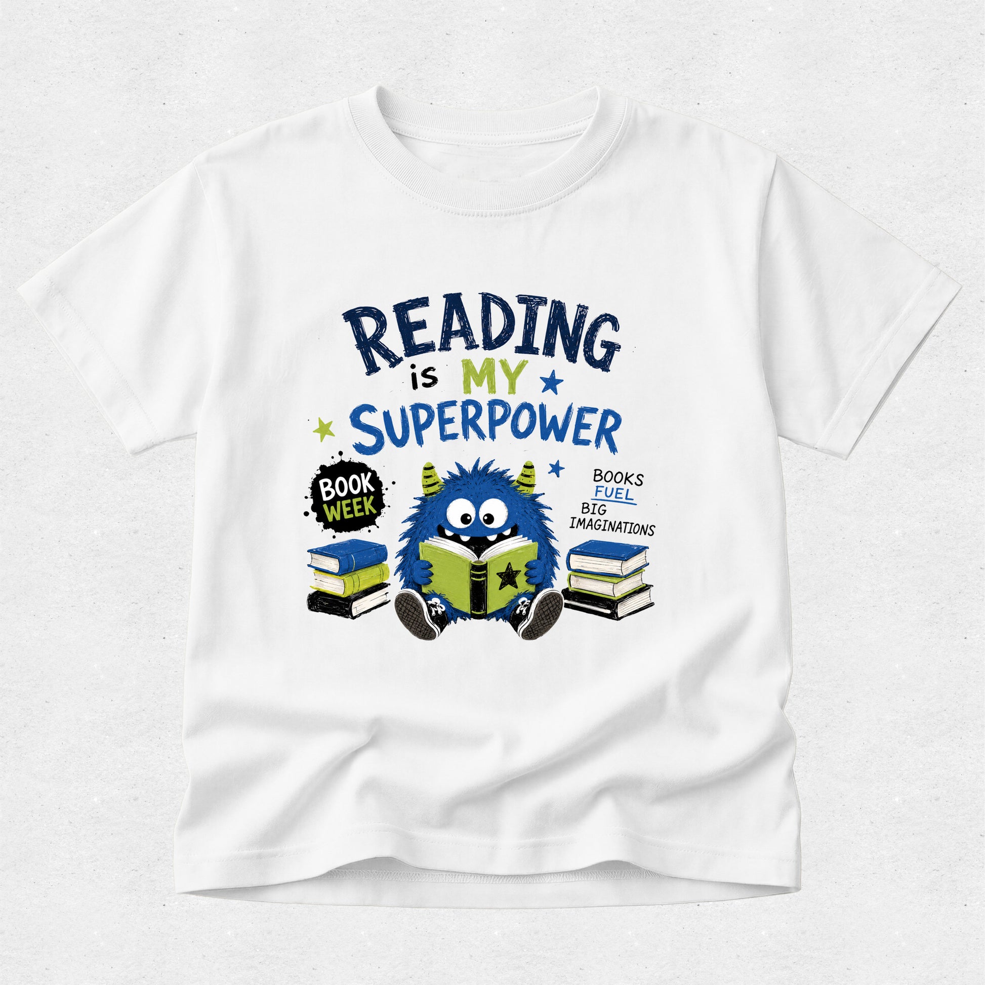 A white short-sleeve crewneck t-shirt featuring a colorful graphic design on the front. The graphic reads 'READING is MY SUPERPOWER' in dark blue and yellow lettering, accompanied by a cute blue monster reading a green book, stacks of books, and a 'BOOK WEEK' badge, all set against a light gray textured background.