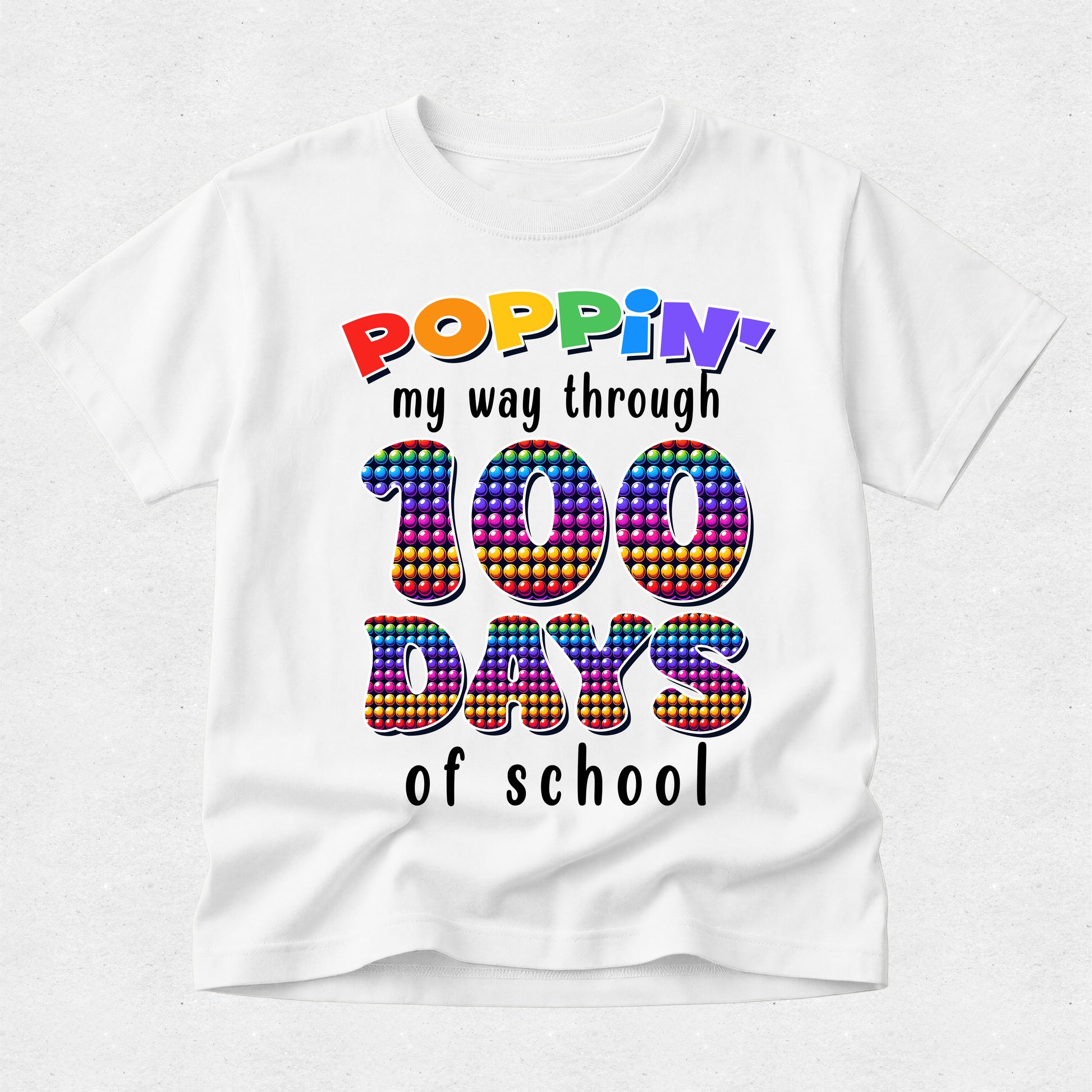 A white short-sleeve t-shirt with a colorful graphic that reads 'POPPIN' my way through 100 DAYS of school' on a light gray background.