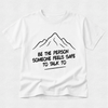 A white short-sleeve t-shirt with a black line drawing of a mountain and the text 'BE THE PERSON SOMEONE FEELS SAFE TO TALK TO' printed on the front, displayed against a light gray textured background.