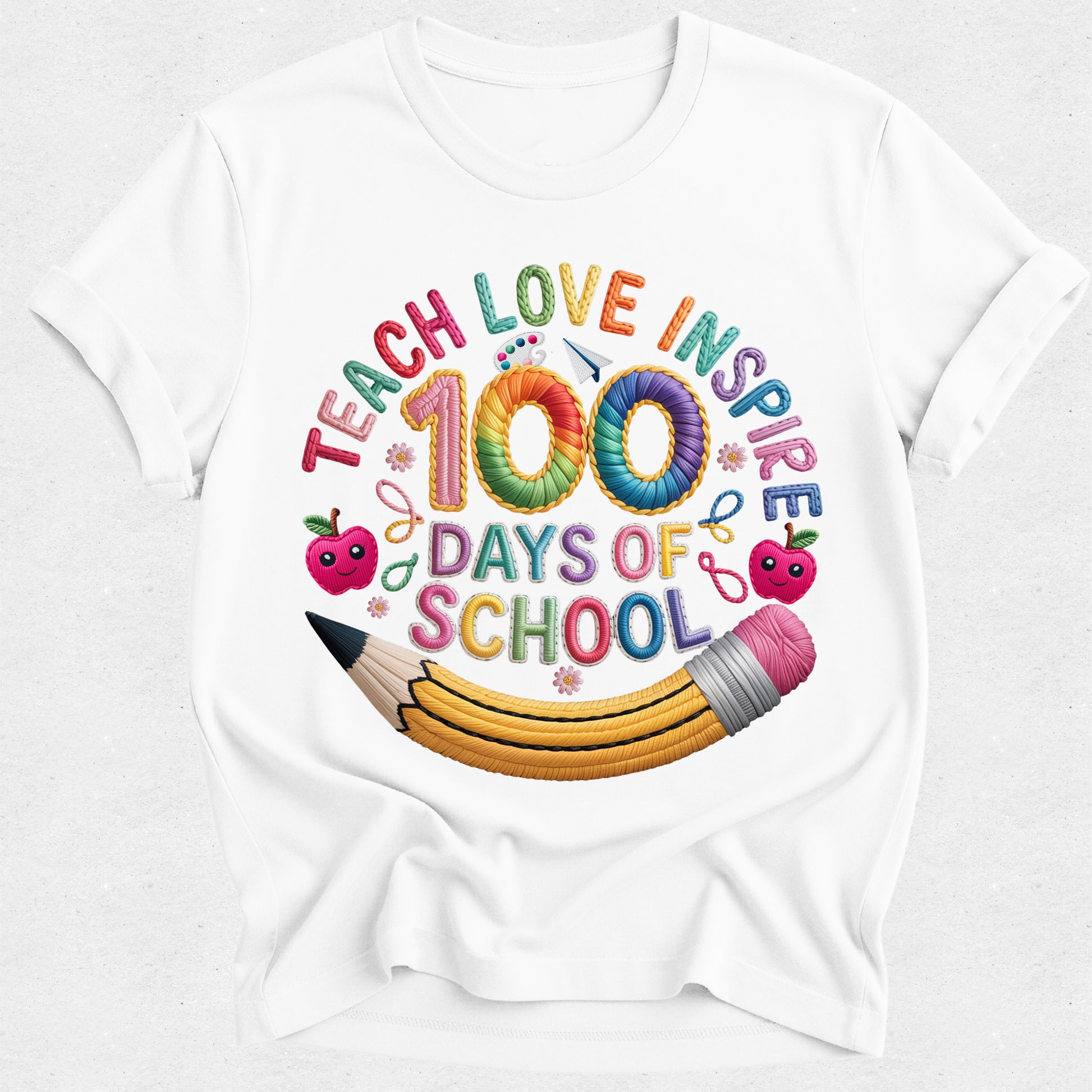 A white short-sleeve crewneck t-shirt featuring a colorful graphic design on the front. The design reads 'TEACH LOVE INSPIRE 100 DAYS OF SCHOOL' in playful, multi-colored lettering, decorated with cartoon apples, a yellow pencil, and small pink flowers.