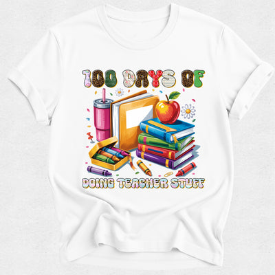 A white short-sleeve crewneck t-shirt featuring a colorful graphic print on the front. The graphic displays school supplies including a stack of books, an apple, a pink drink, crayons, and a pencil, with the text '100 DAYS OF DOING TEACHER STUFF' written above and below the illustration.