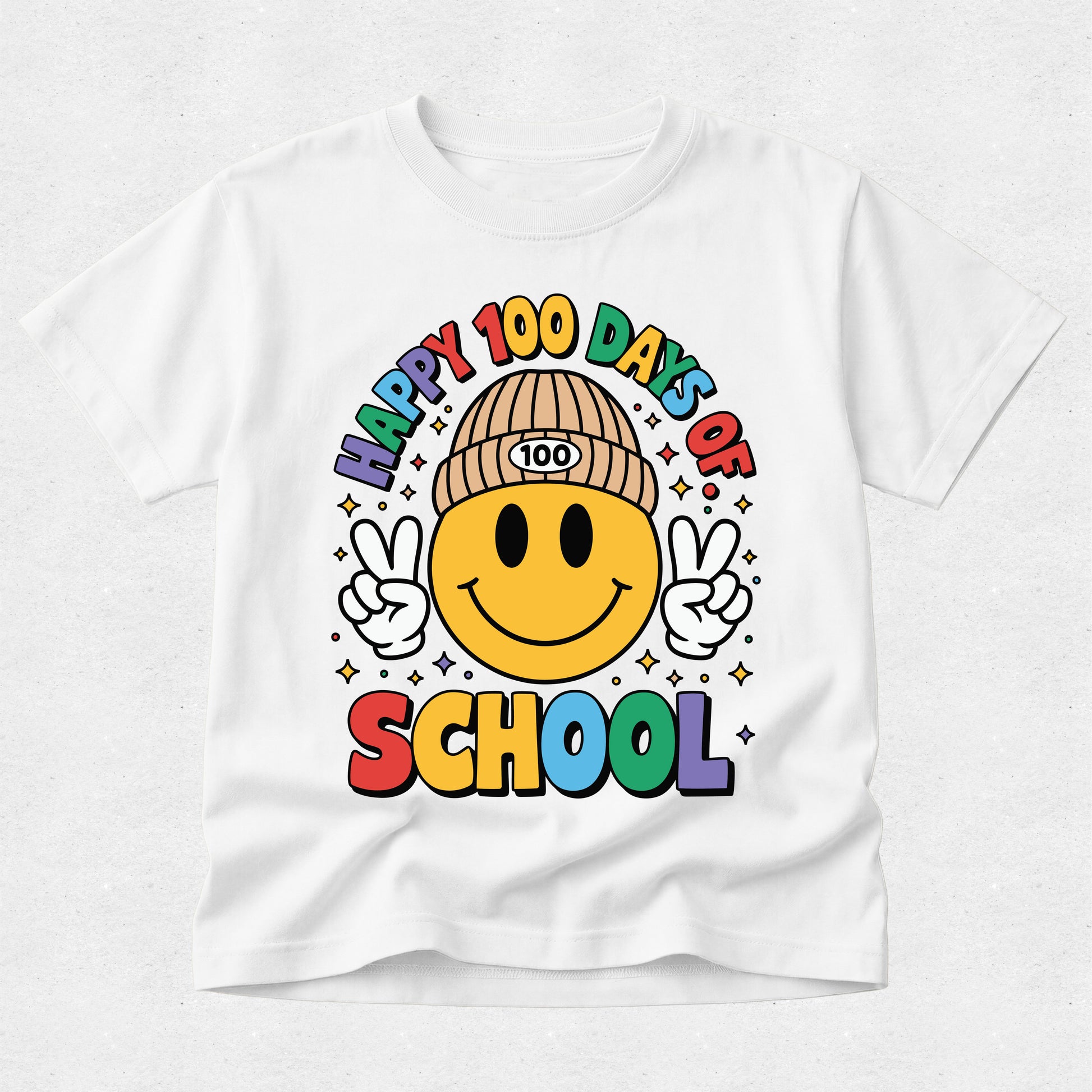 A white short-sleeve t-shirt with a colorful graphic on the front that reads 'HAPPY 100 DAYS OF SCHOOL' around a smiling face wearing a beanie with '100' on it, set against a light gray textured background.