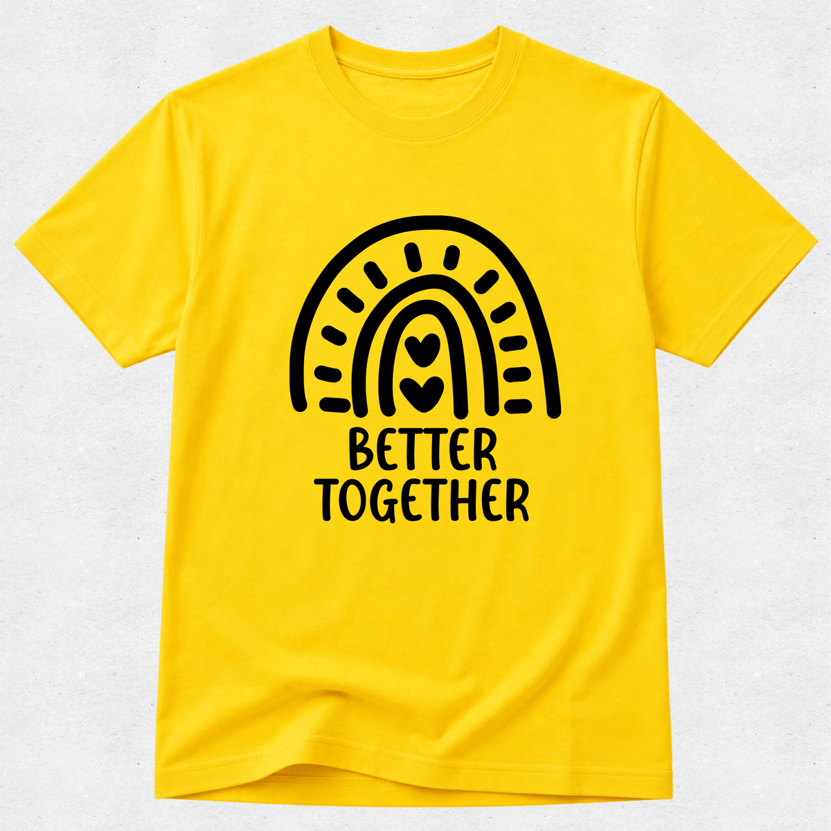 A bright yellow short-sleeve t-shirt with a black graphic of a rainbow arching over the words 'BETTER TOGETHER' in a rounded block font. The t-shirt is displayed flat against a light gray textured background.