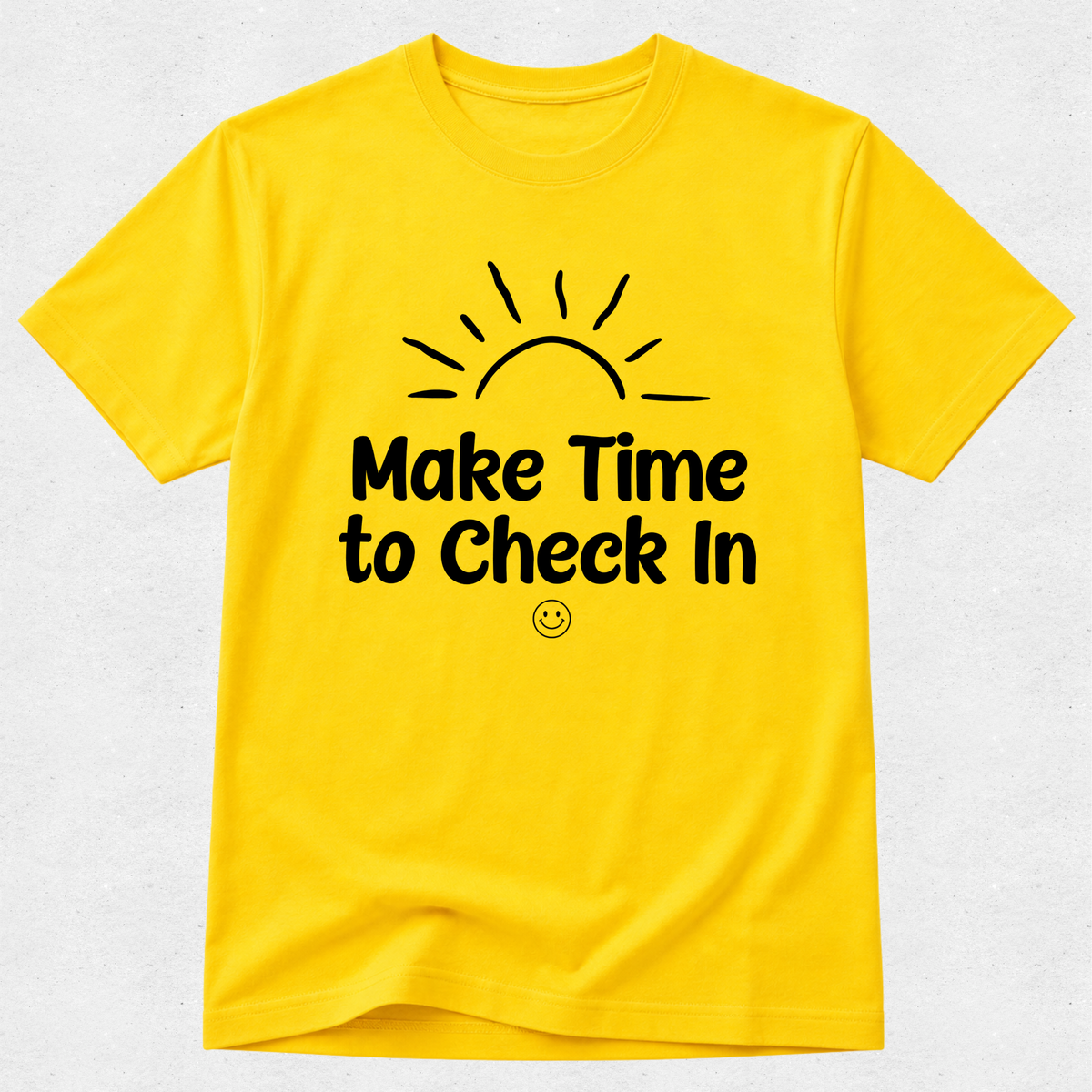 A bright yellow short-sleeve crewneck t-shirt with a black graphic print on the front showing a rising sun and the text 'Make Time to Check In' with a small smiley face underneath, displayed on a light gray textured background.