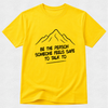 A bright yellow short-sleeve t-shirt with a black line drawing of a mountain and the text 'BE THE PERSON SOMEONE FEELS SAFE TO TALK TO' printed on the front, displayed against a light gray textured background.