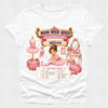 A white short-sleeve crewneck t-shirt featuring a detailed pink graphic print for a 'Book Week Quest' ballerina studio theme, with a checklist at the bottom and the name 'Megan' printed on a banner.