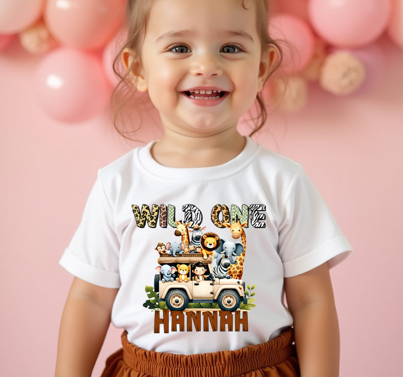 Child wearing a 'Wild One' t-shirt with a safari design on a pink background