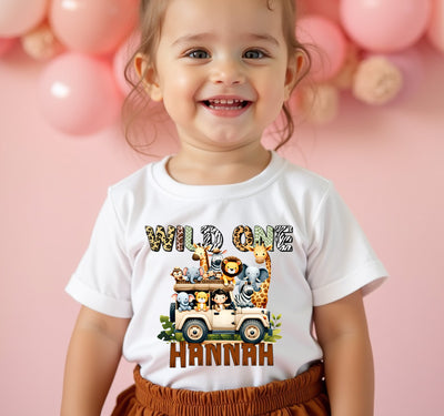 Child wearing a 'Wild One' t-shirt with a safari design on a pink background